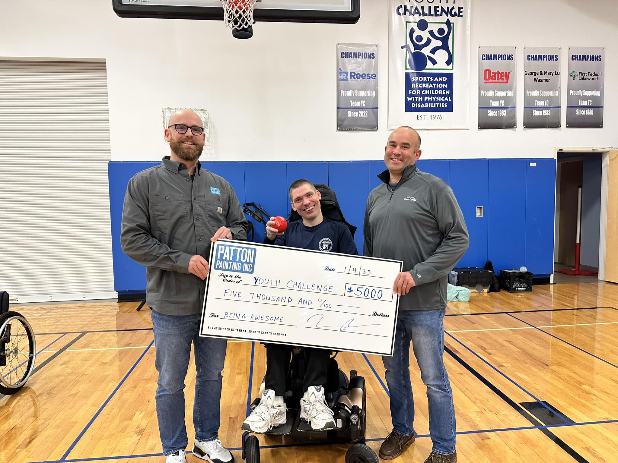 Three people holding a large check made out to youth challenge in a basketball court
