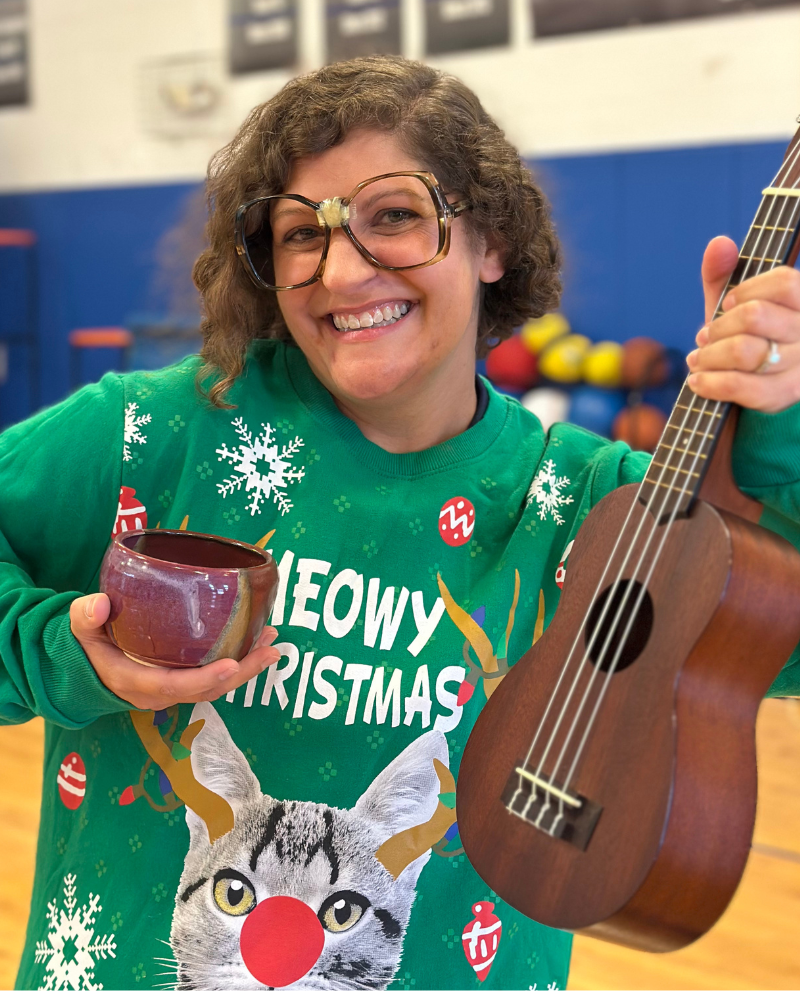 Sarah Cooney wearing a holiday sweater and silly glasses, holding accessories.