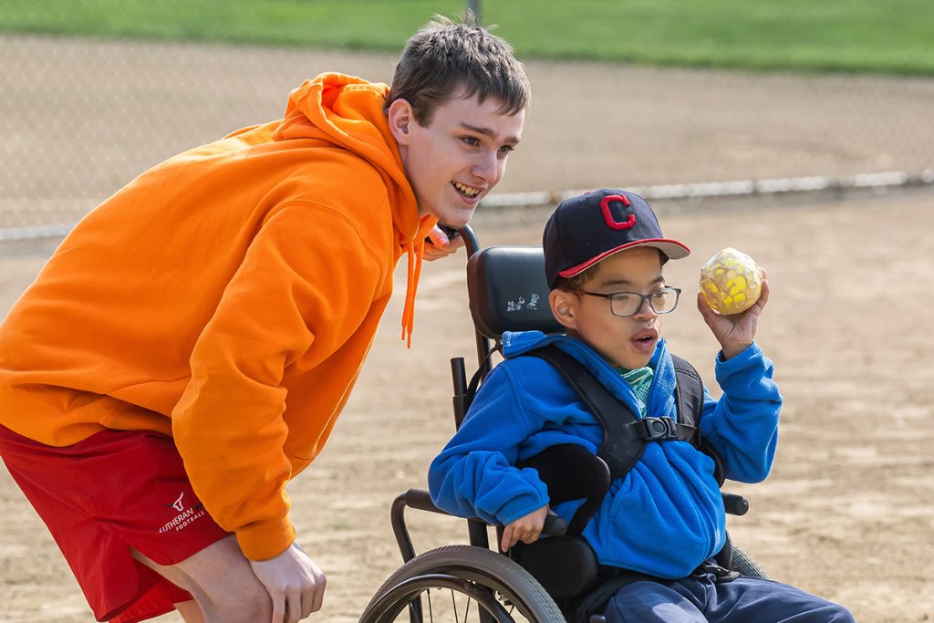 A volunteer and participant play baseball.