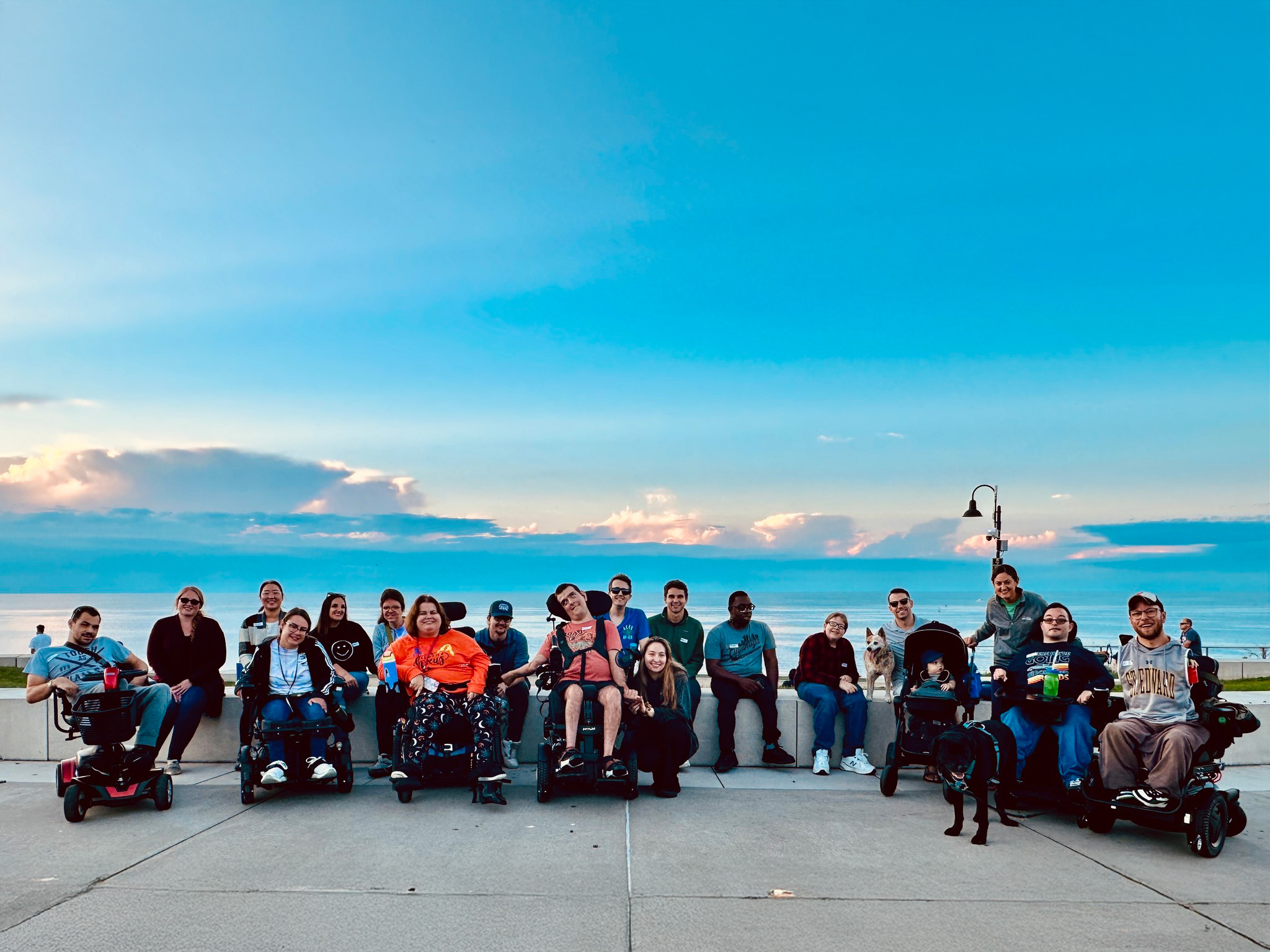 a group of people posing for a picture in front of the lake with a beautiful blue sky