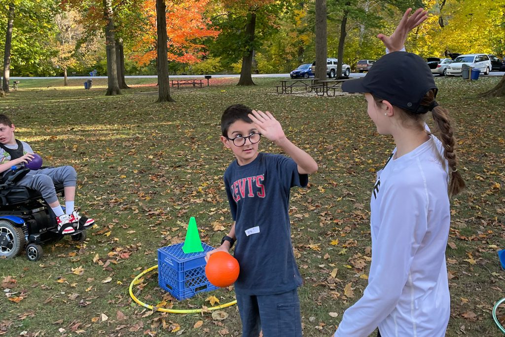 Kid holding a ball high fiving a girl with fall trees behind