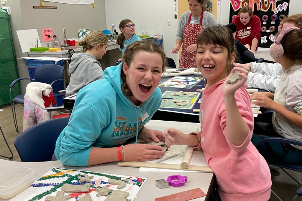 A teen with a young girl at a table doing crafts