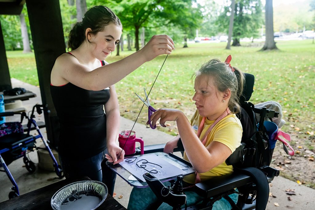 Teen pulling a piece of string as a girl in a wheelchair cuts it with scissors