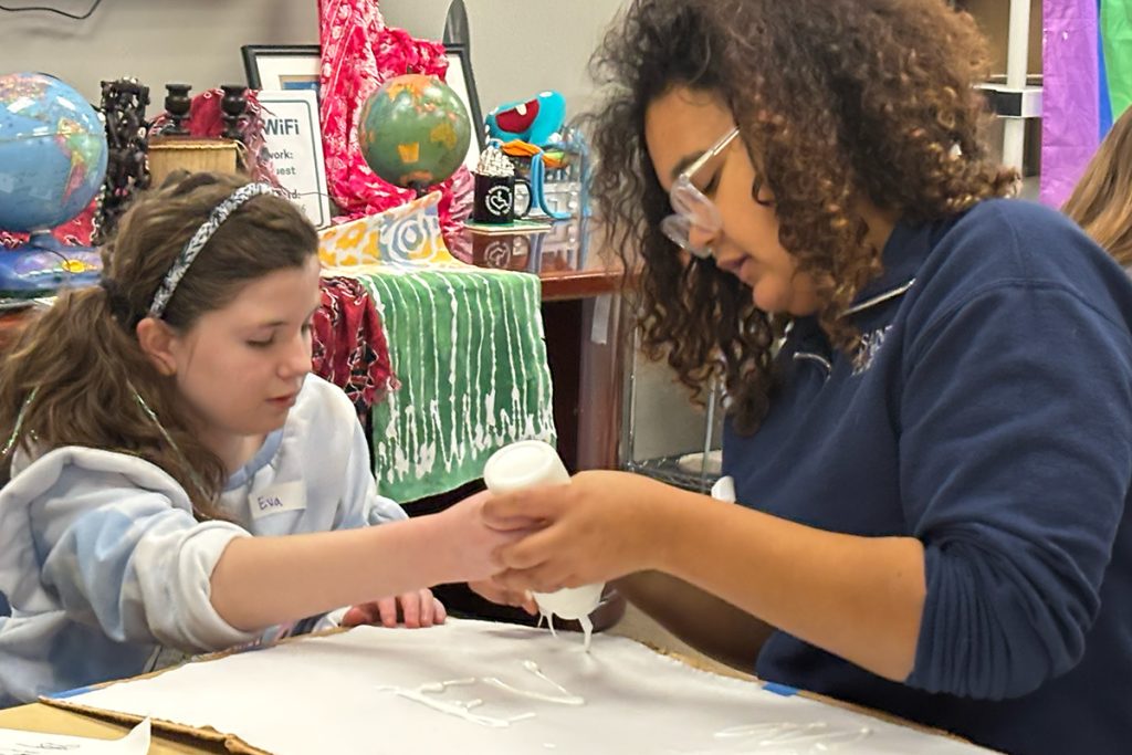 Teen and girl using a bottle on a piece of paper doing crafts