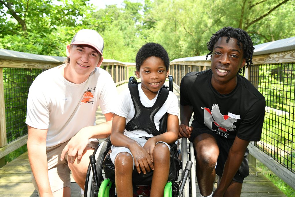 Two teens flanking a boy in a wheelchair outside