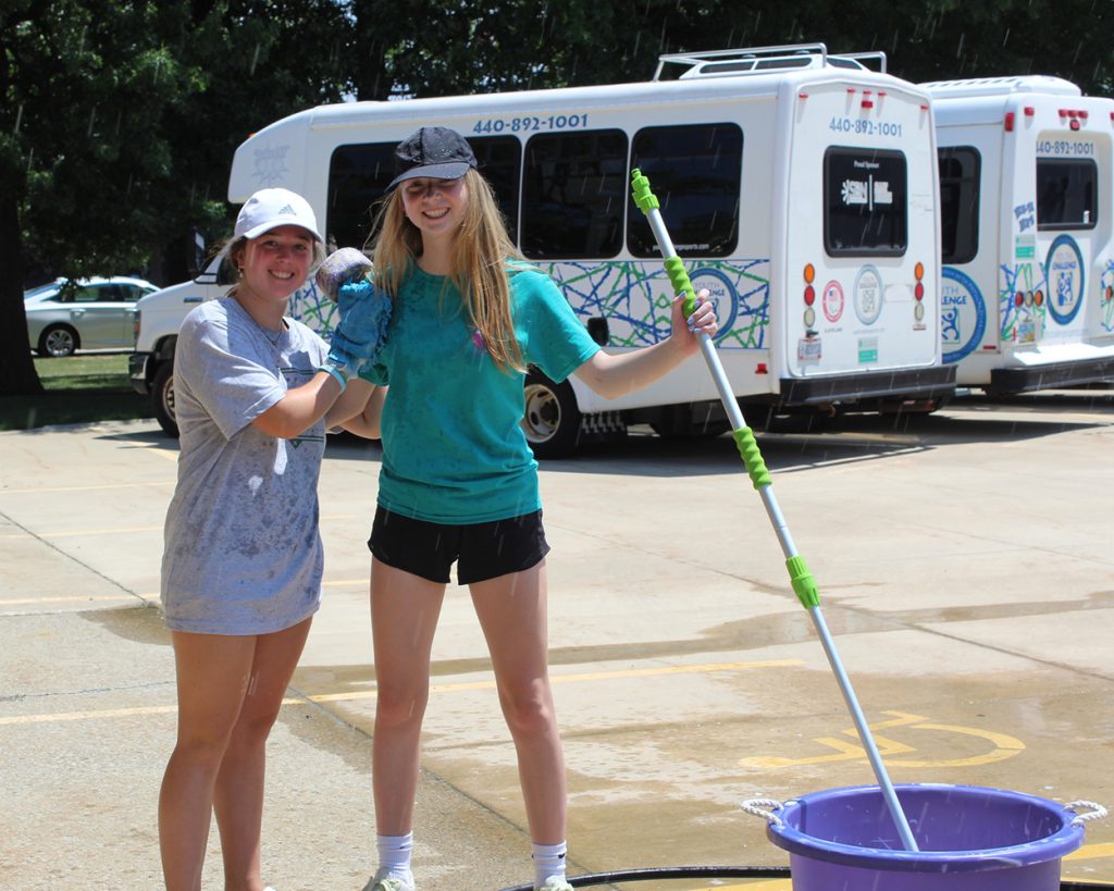 Two teens standing in front of some vans with a mop and a bucket