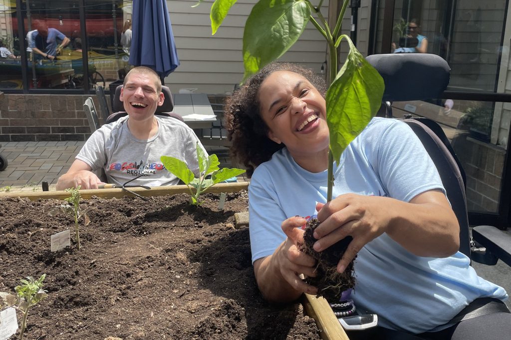 Two people sitting at a raised bed gardening, one holding a plant