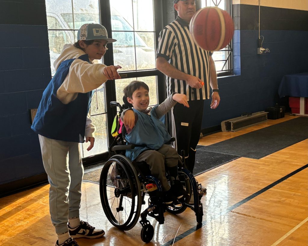 Teenager coaching a child in a wheelchair throwing in a basketball
