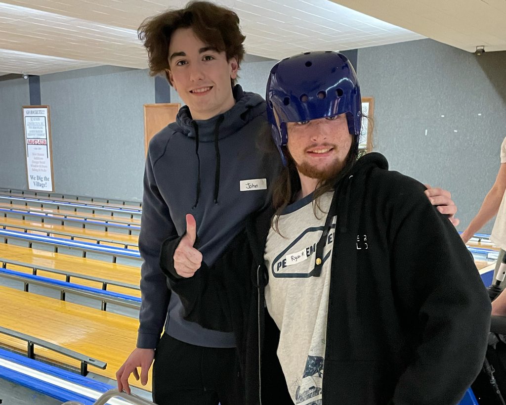 Two young men standing together with bowling alleys behind