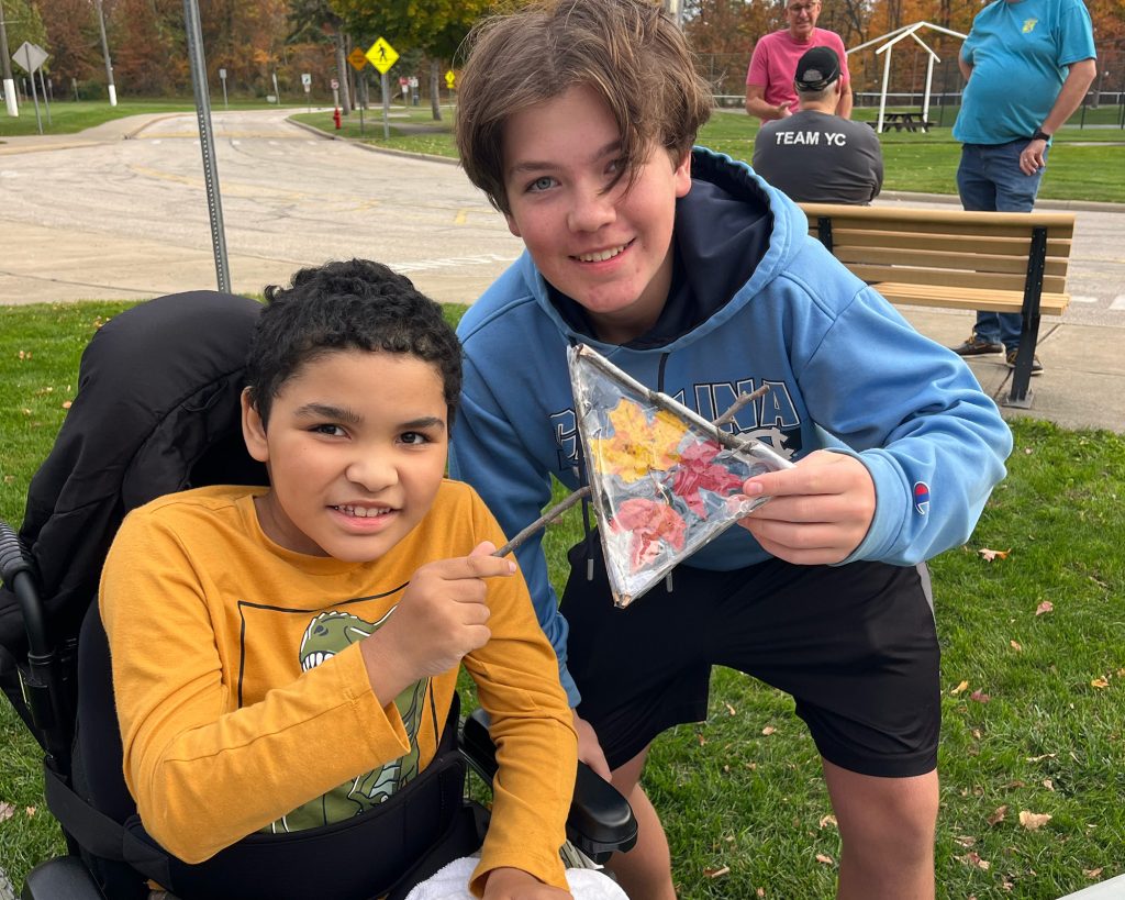 A teen holding a ceramic piece next to a child sitting down