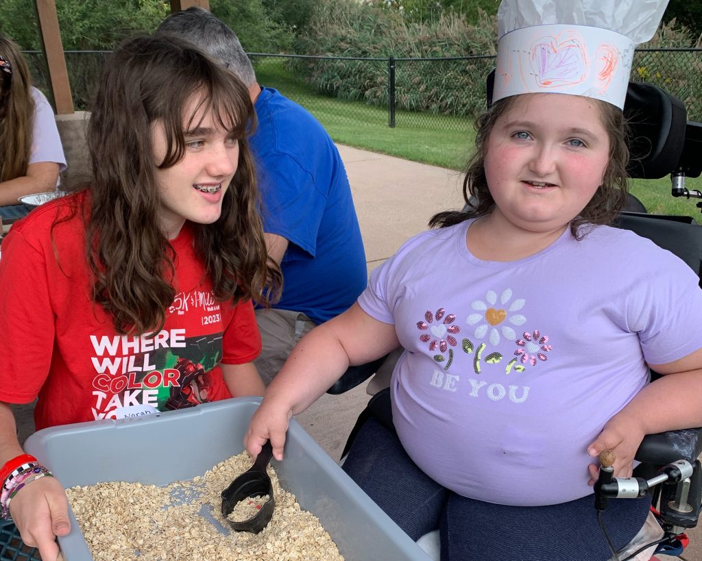 A teenager holding a dish of food with a kid wearing a chef's hat