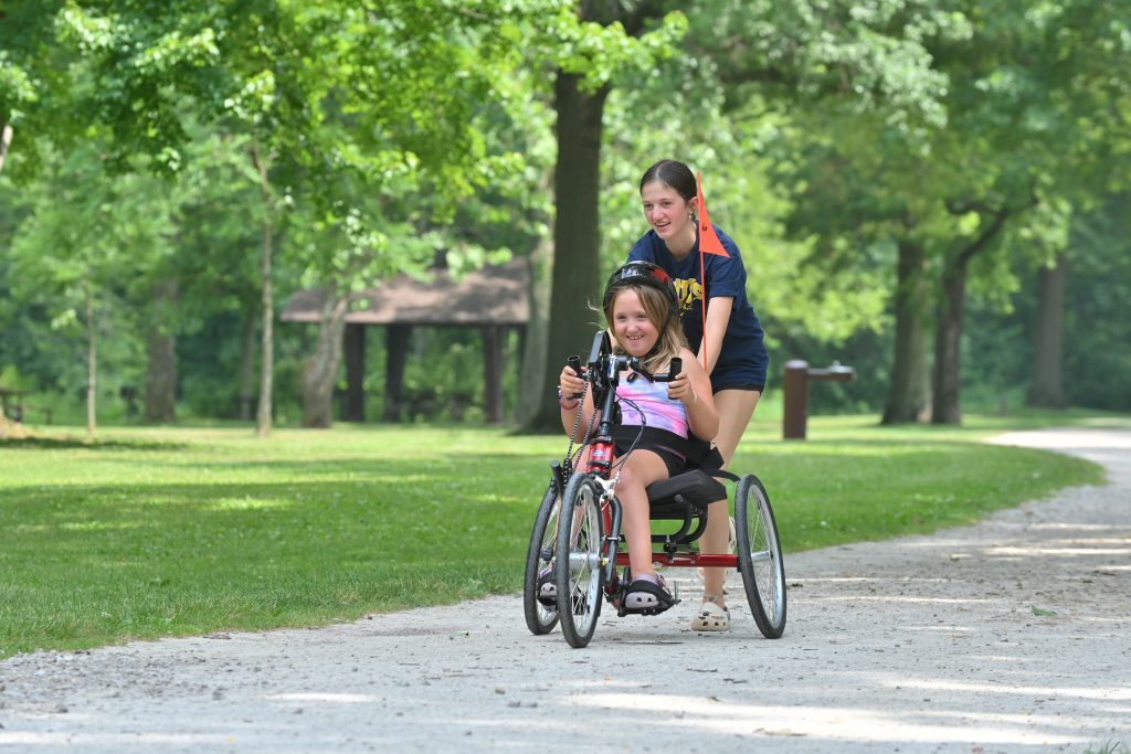 A teen helping a child in an accessible bicycle