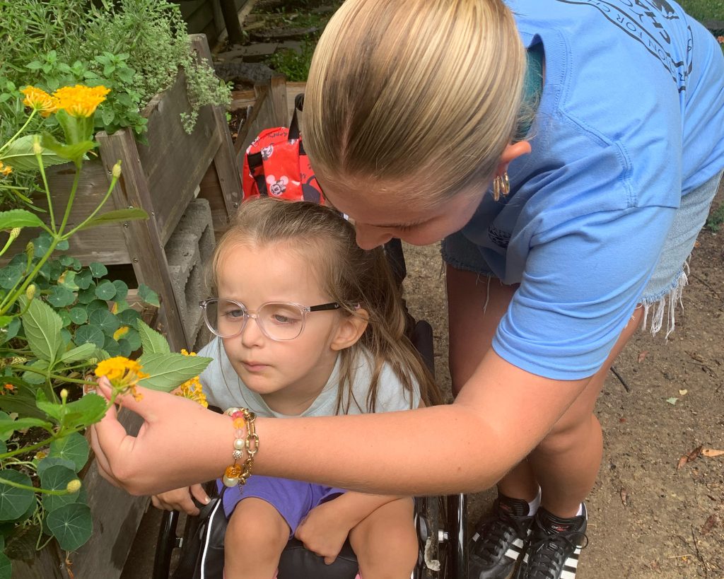 a child with glasses being helped in a garden by an adult