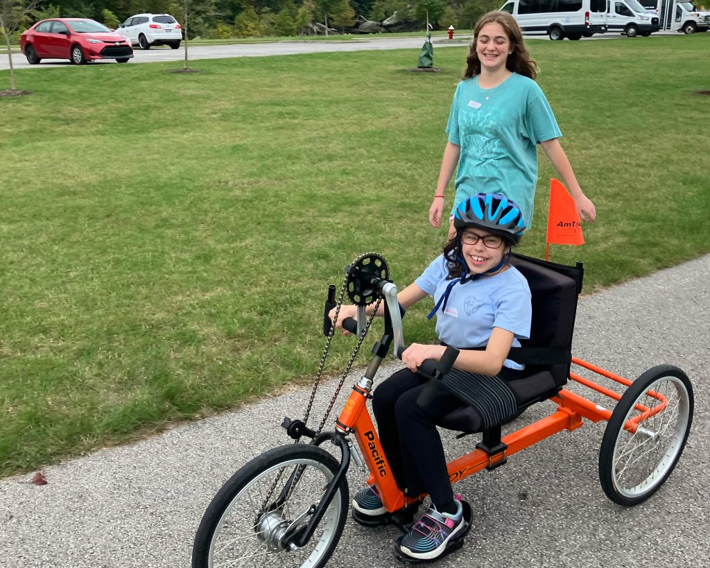 A child using a handcycling bike with another standing behind
