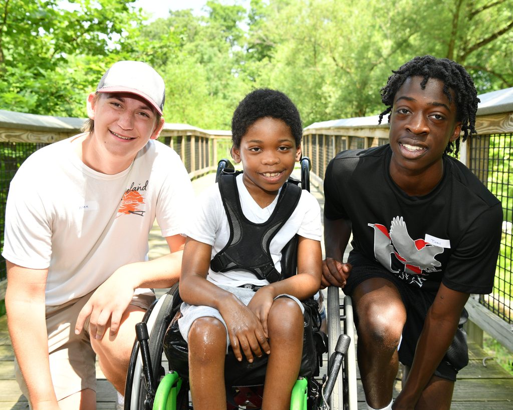 Two teens flanking a child sitting in a wheelchair