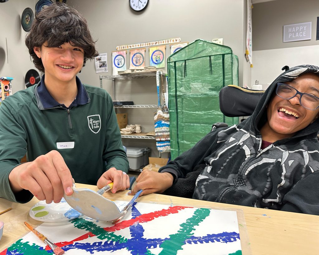 2 kids sitting at a table painting both laughing