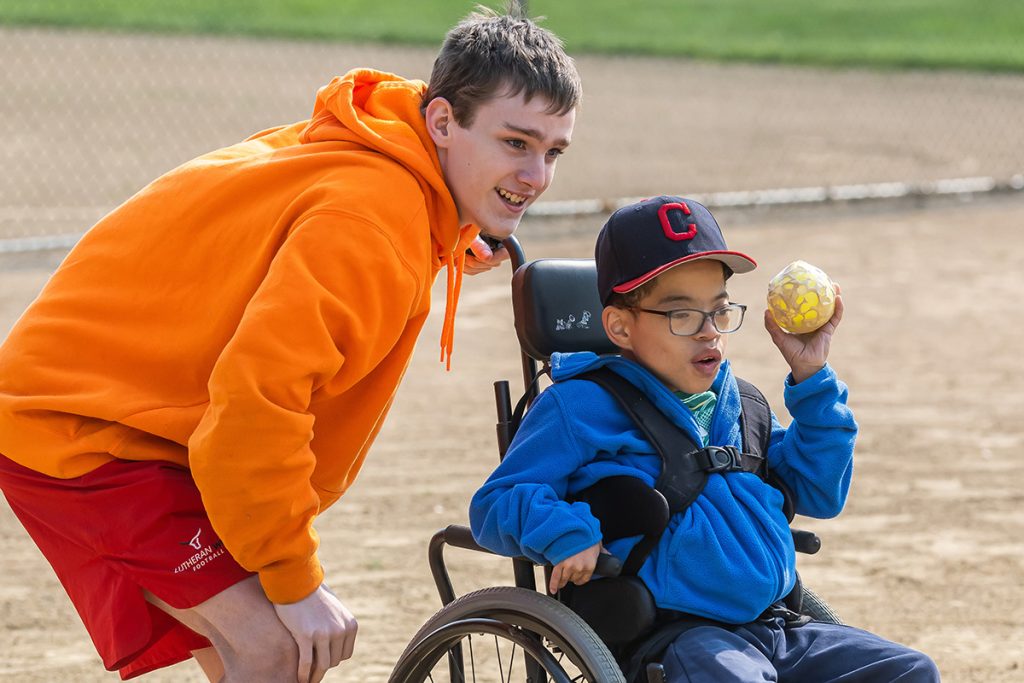 Boy in orange hoodie playing with a kid in a wheelchair
