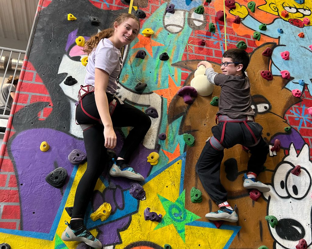 A girl and child using a very colorful rock wall to climb