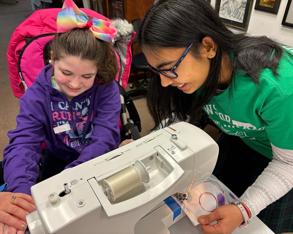 A participant and a teen using a sewing machine together