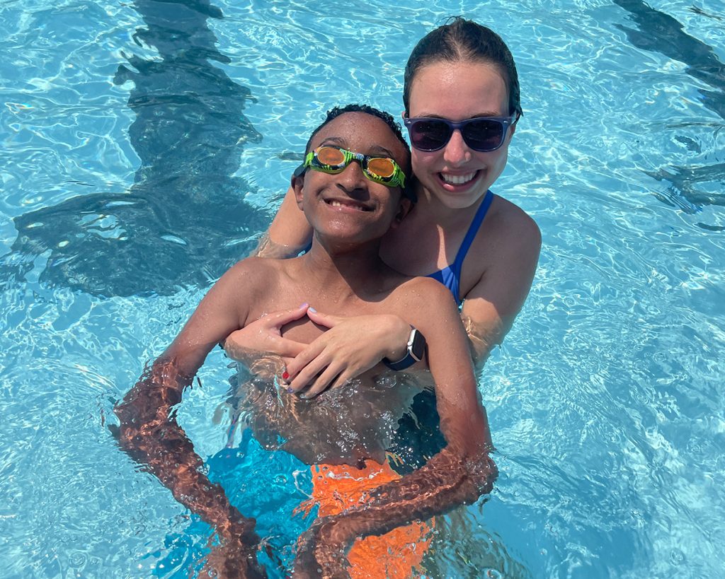 A lady holding a participant youth in a pool
