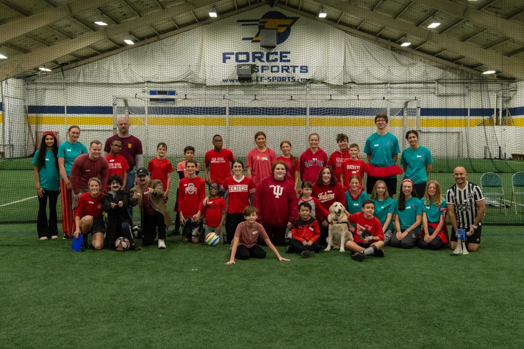 A large group of kids in red and green shirts inside of an inside sports facility