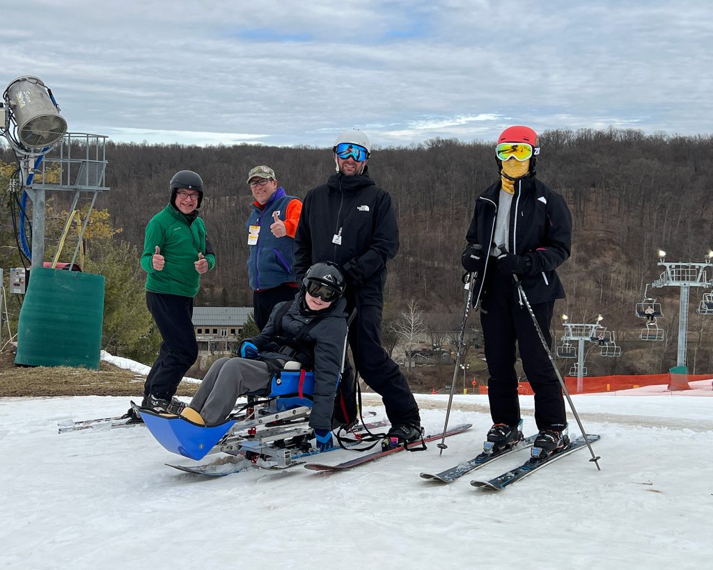 4 people at the top of a ski hill with an accessible skier