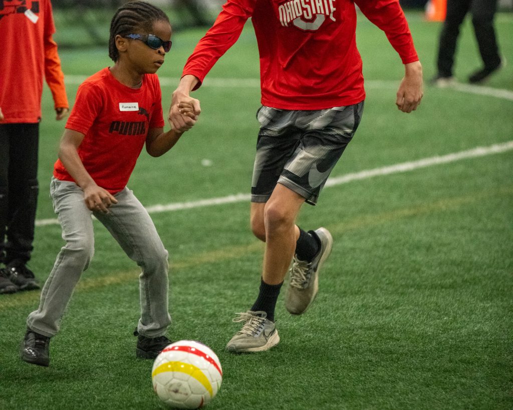 a blind boy playing soccer while holding a mans hand