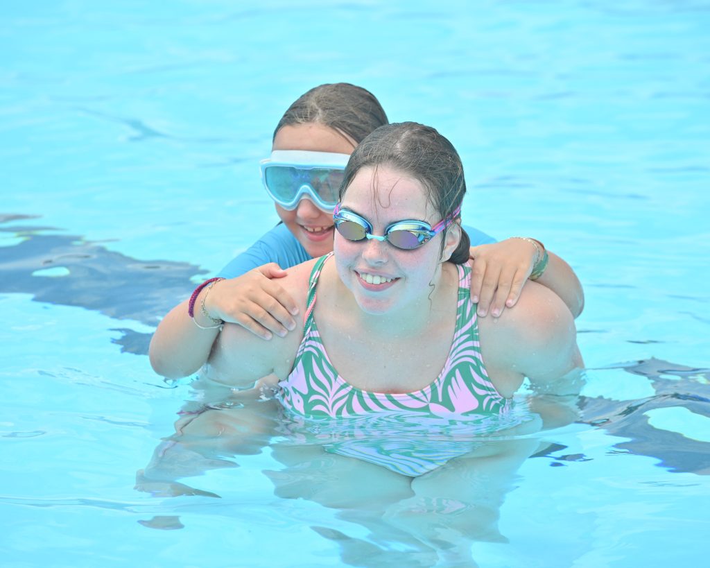 A teenager holding a child on her back in a pool