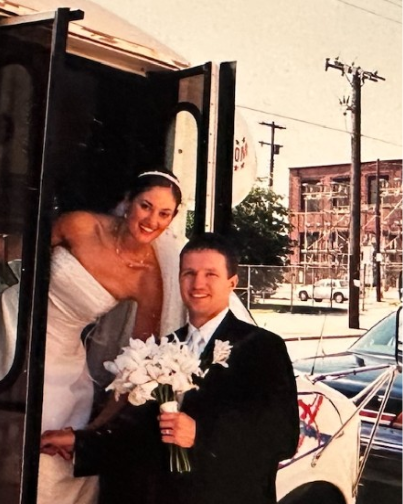A woman in a bus door in a wedding dress and a man in a tux holding flowers