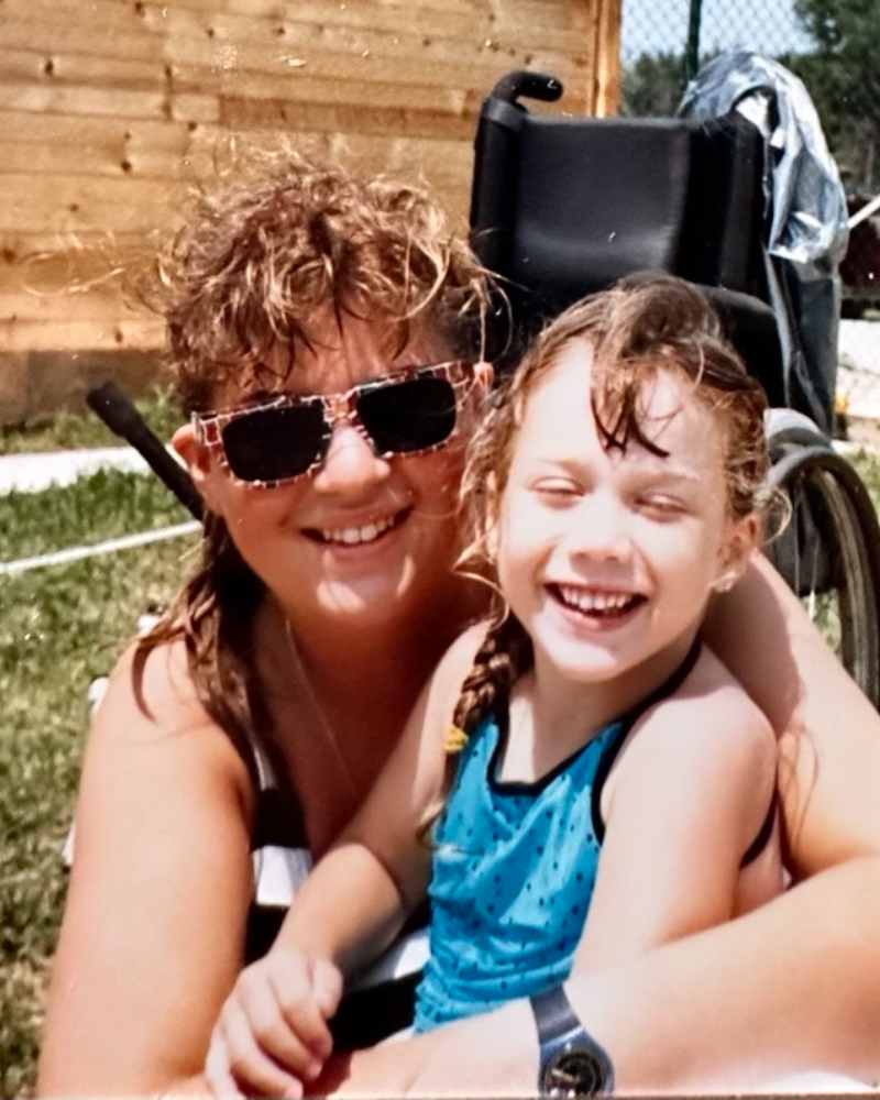 Sharon Douglas with glasses on holding a child smiling