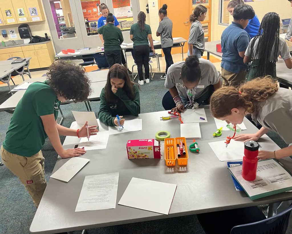 A group of people heads down at a table writing on paper.