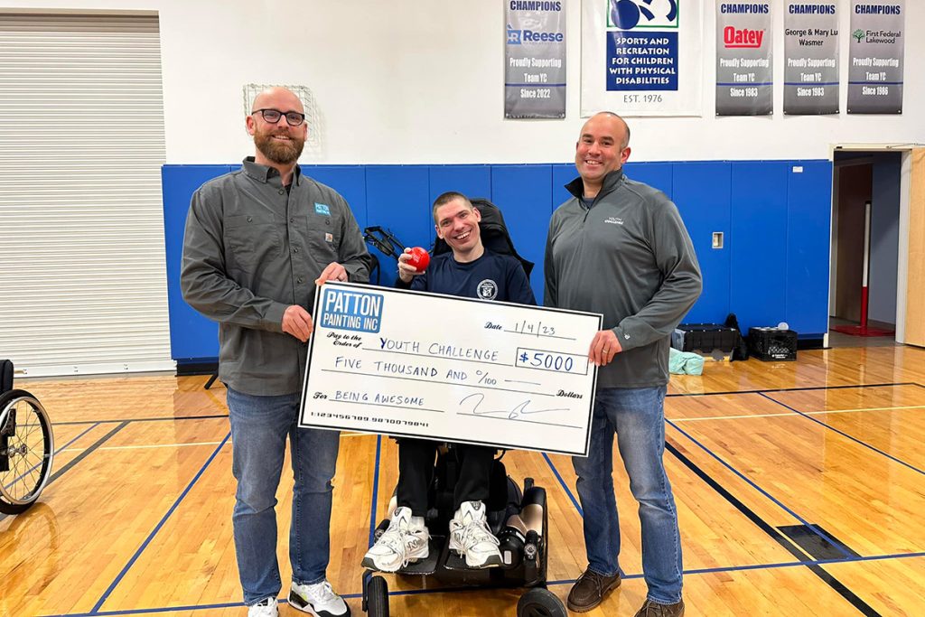 Two men flanking a man in a wheelchair holding a giant check