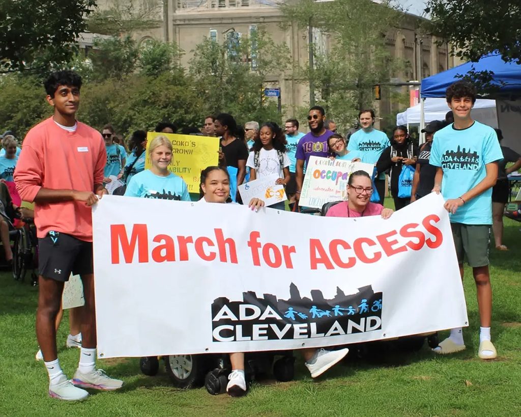 A group of people outside holding a sign saying "March for Access"
