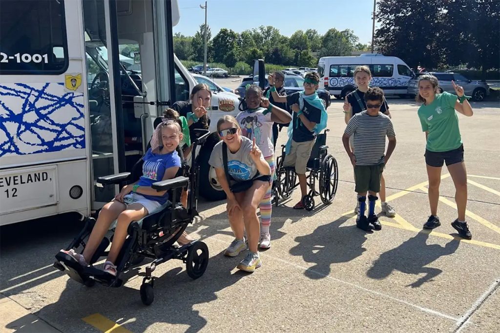 A group of kids, some in wheelchairs outside of a van on a sunny day