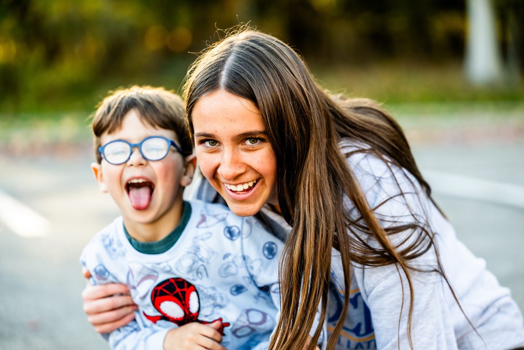 A teen holding a boy with blue glasses posing for the camera