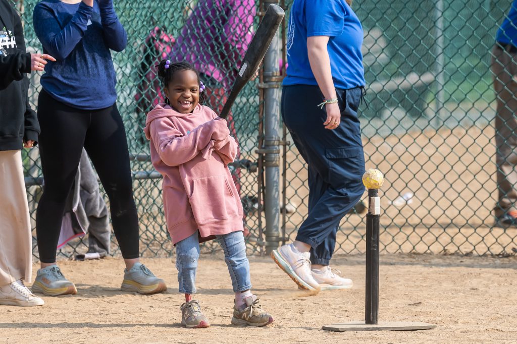 A girl in a pink hoodie holding a bat playing teeball