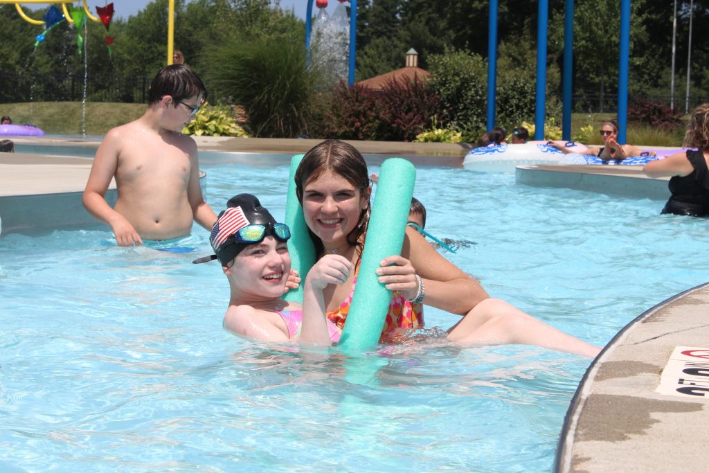 a teen helping a kid sitting in a pool noodle having fun in a pool