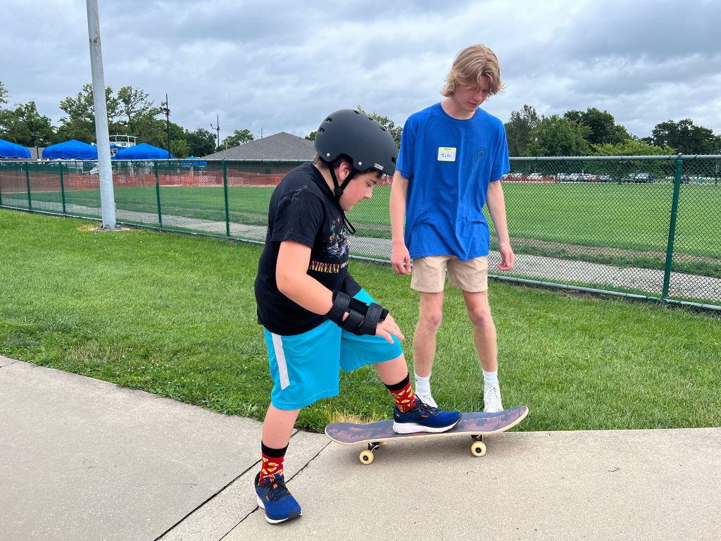 A teen in a blue shirt encouraging a child who is skateboarding
