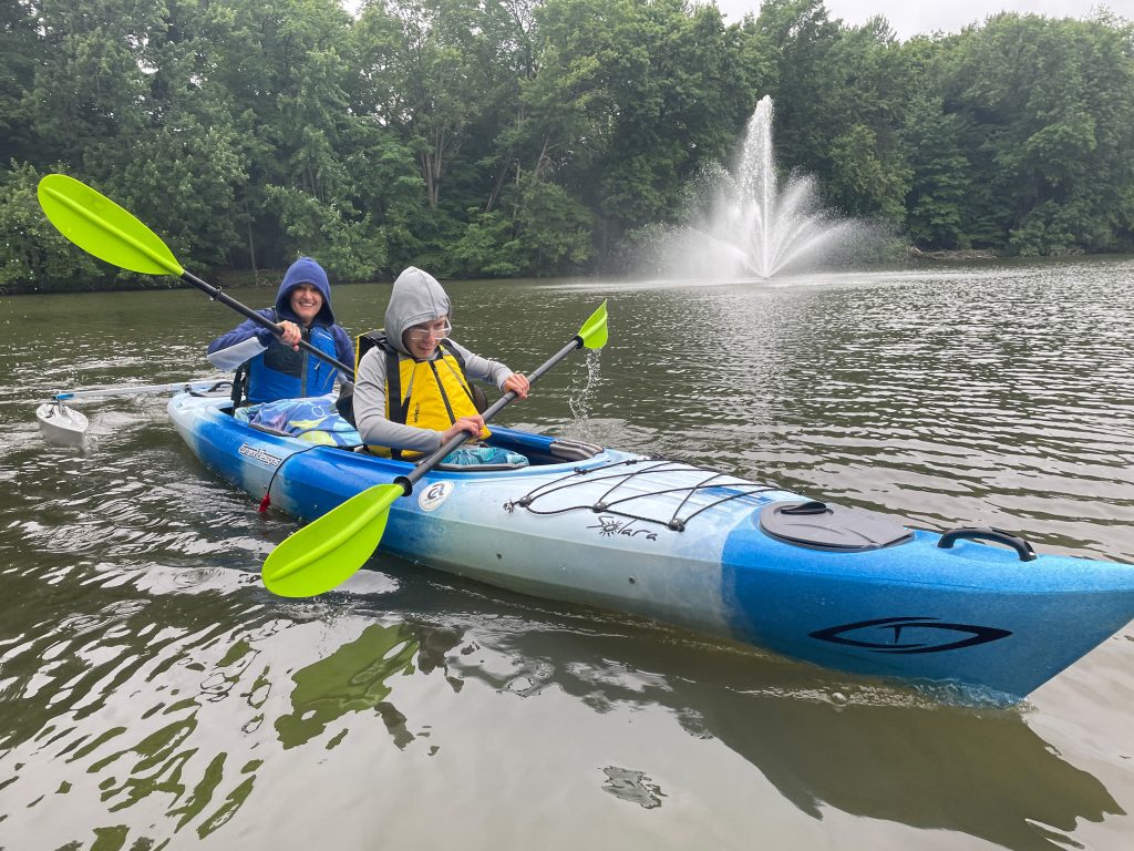 Two people wearing hoods in a kayak in a little pond