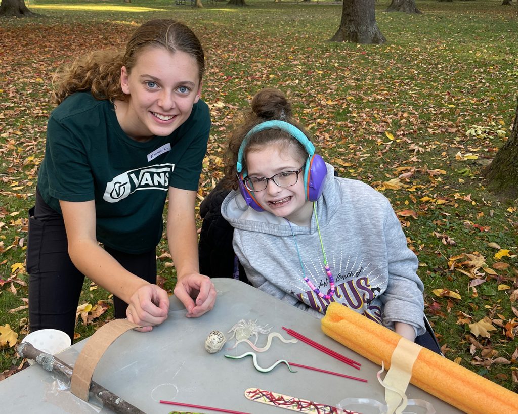 A teen helping a child with headphones on at a table outside
