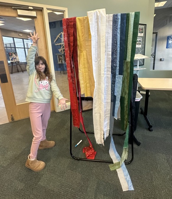 A female participant poses next to finished quilt sections hanging on an easel.