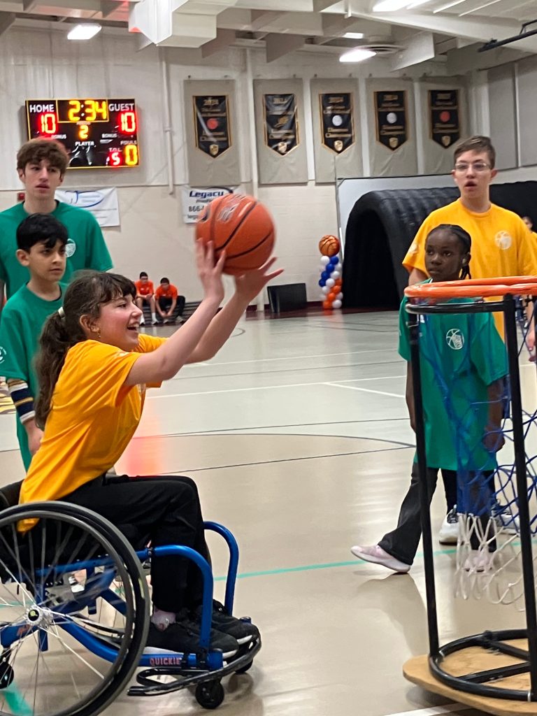 teen girl in wheelchair gets ready to make basket, members of both teams watch her