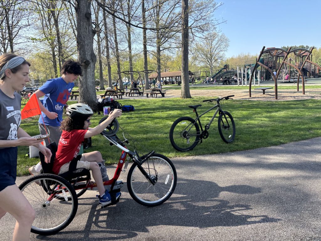 Participant races on hand cycle with staff member and volunteer on either side.