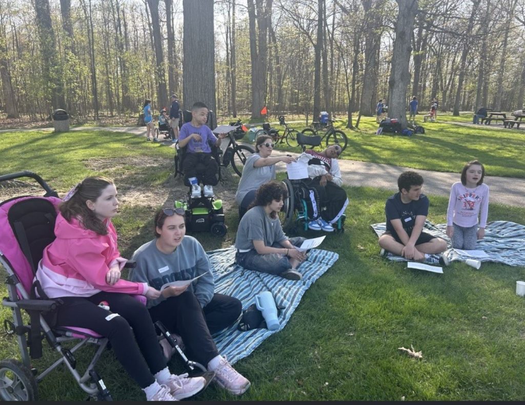 Participants and volunteers hold music sheets and sing together in a park.