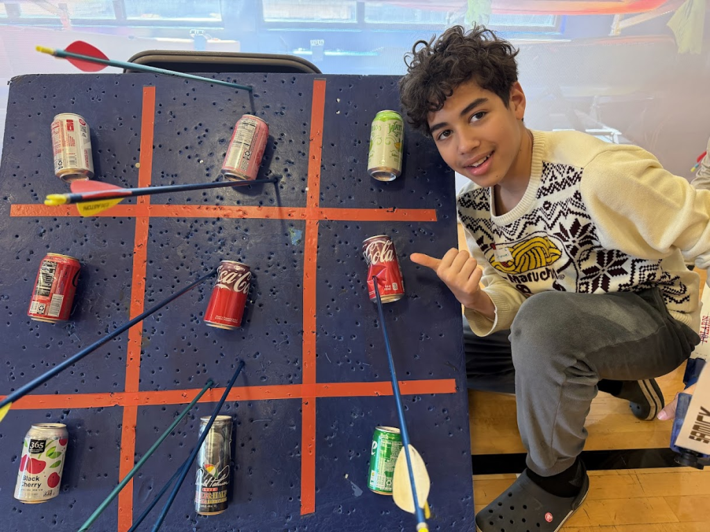 young man poses next to an archey target with arrows piercing pop cans