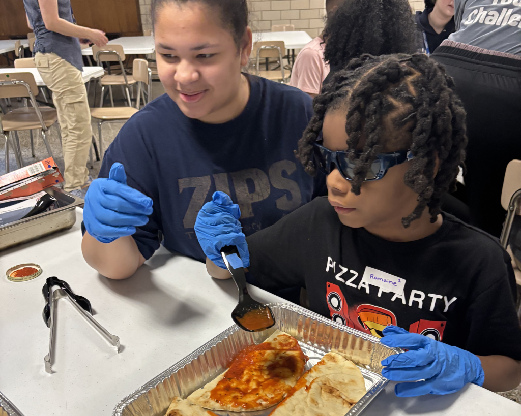 A teen volunteer and participant smile while making pasta