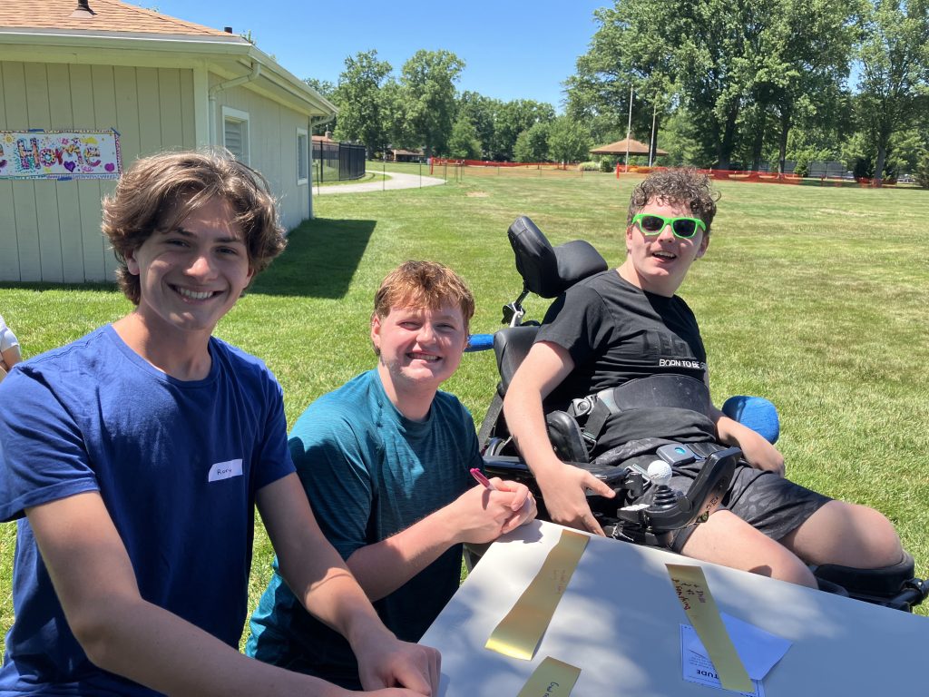 Three boys smiling at a program in the grass.