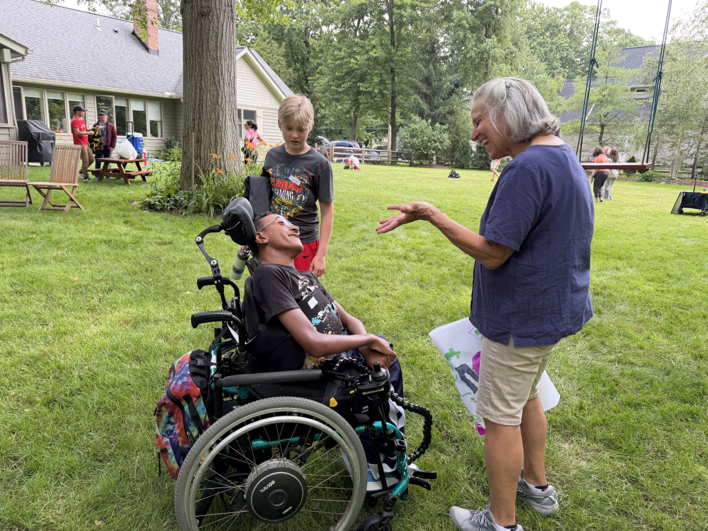 YC founder Mary Sue spraks to participant in wheelchair as his volunteer stands next to him.