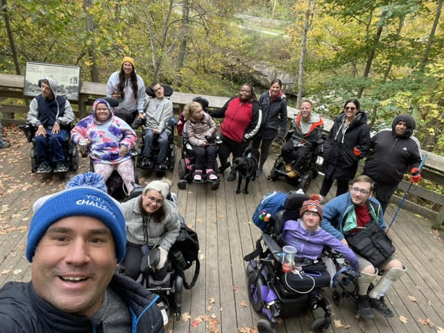 A group of people standing and sitting in wheelchairs posing for a photo on a nature walk
